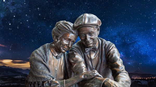 Statues of an elderly couple resting on each other with a decorative starry background